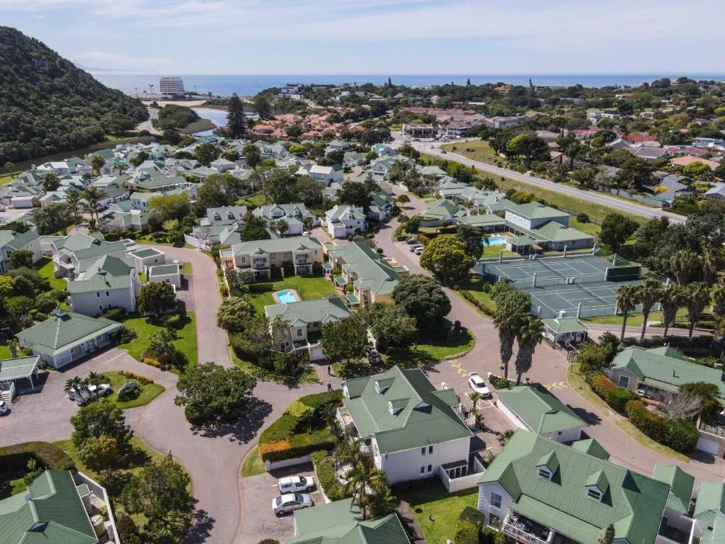Aerial view of the gated estate showing tennis courts, a shared pool and tiled rooftops toward the sea