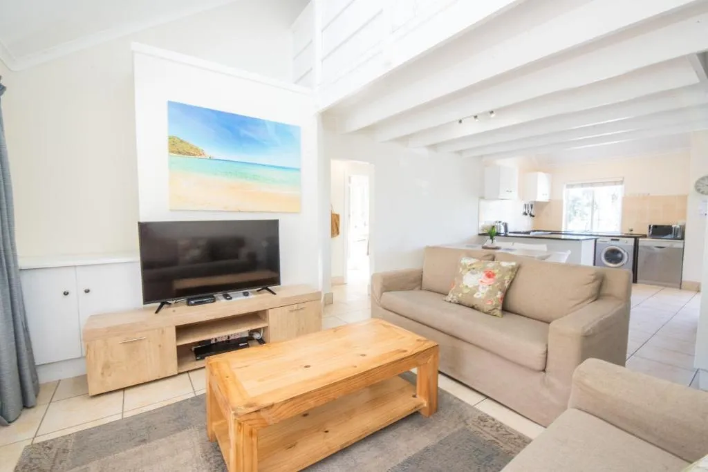 Living room with a beach-themed canvas, TV and an open kitchen with a dishwasher and washing machine