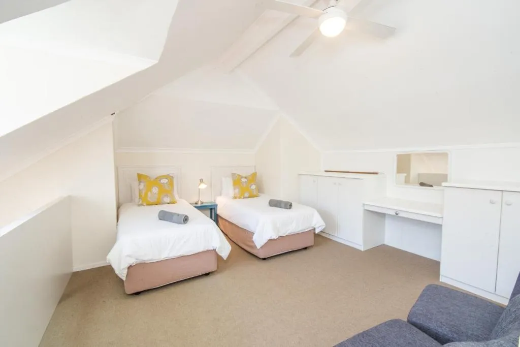 Loft twin bedroom under a pitched ceiling with a ceiling fan and built-in cupboards