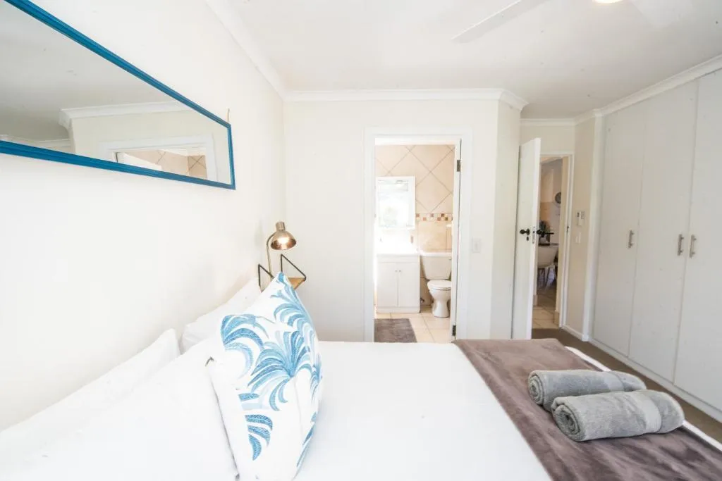 Main bedroom with a blue-framed mirror, fitted wardrobes and an en-suite bathroom beyond