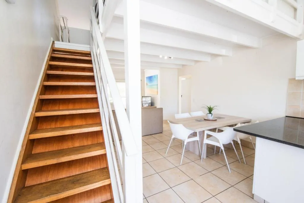 Timber staircase to the loft beside an open dining table and a glimpse of the lounge
