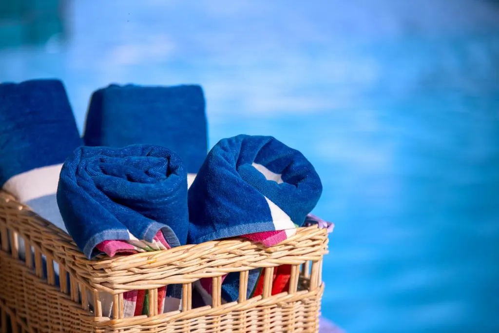 Rolled beach towels in a wicker basket beside the pool's blue water
