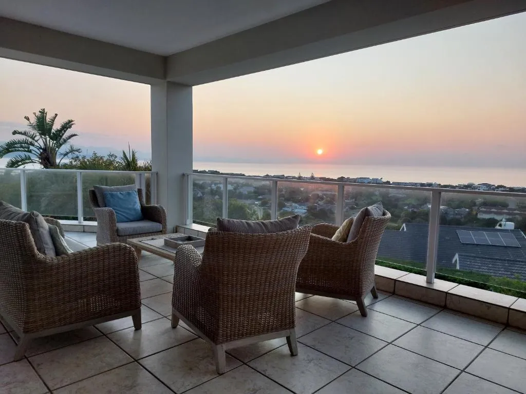 Covered terrace with wicker lounge seating facing the ocean during a vivid sunset