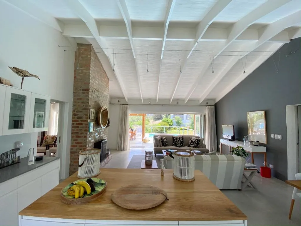 Kitchen island in the foreground opens onto a living room with an exposed brick fireplace and pool doors beyond