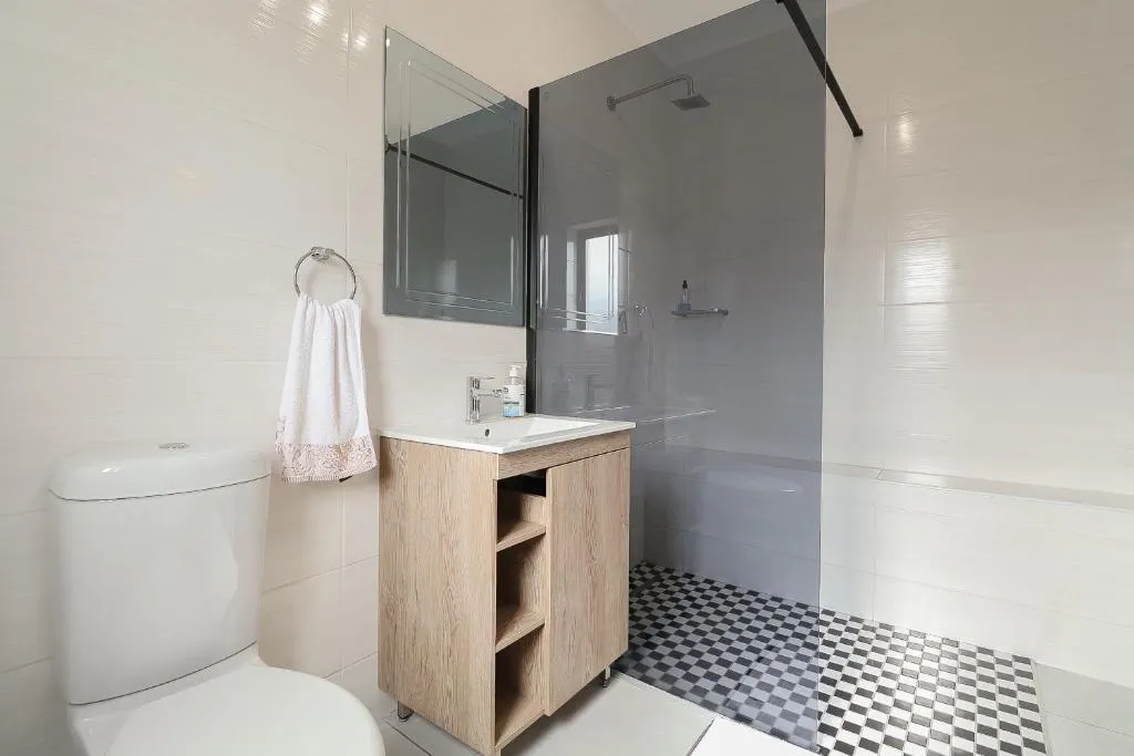 Bathroom with a glass-walled shower, checkerboard floor tiles and wooden vanity