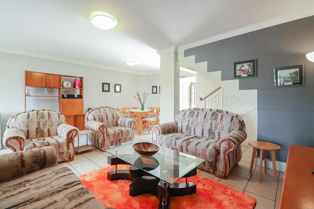 Living room with patterned armchairs, glass coffee table and a staircase to the upper level