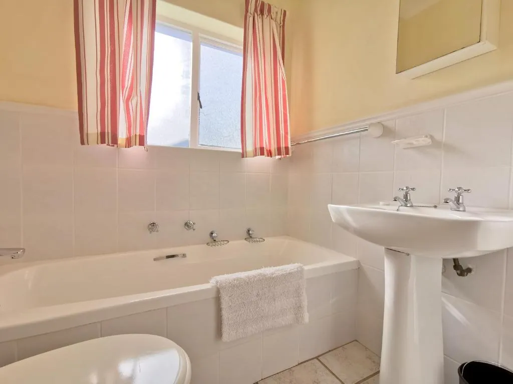 Bathroom with a full-length tub, curtained window and pedestal sink