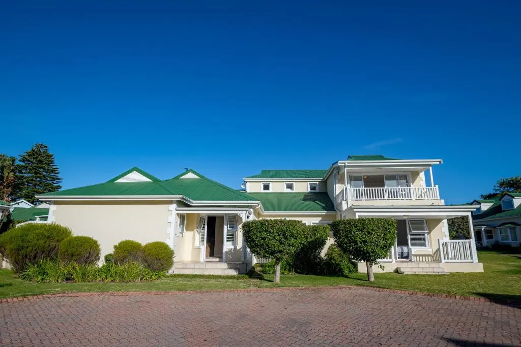Double-storey Cape-style house with a green corrugated roof, white balconies and a paved driveway