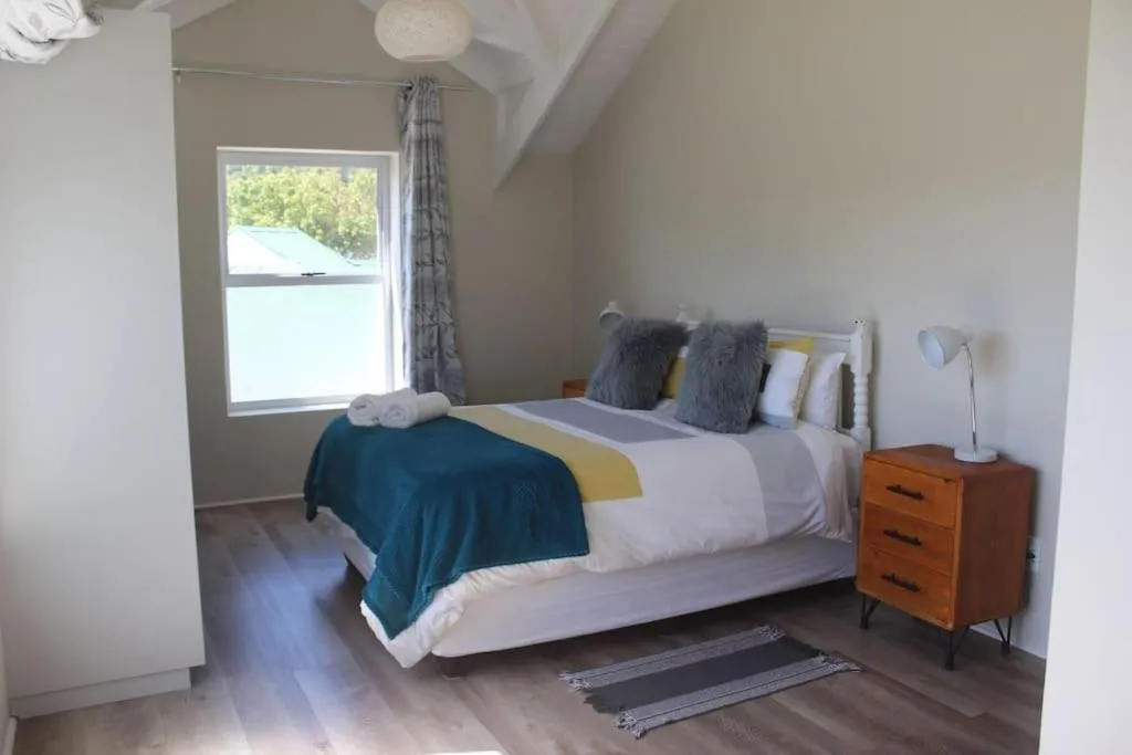 Bedroom with teal throw, grey cushions and a window onto neighbouring rooftops