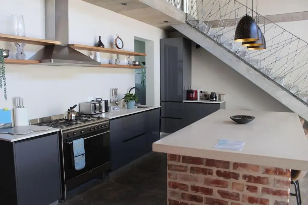 Open-plan kitchen with gas stove, timber shelving and a brick-clad breakfast counter