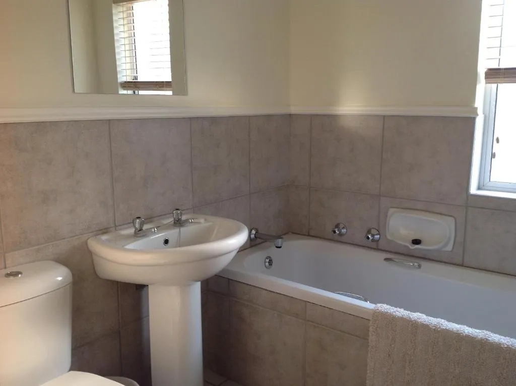 Tiled bathroom with pedestal basin, mirror and a full-length bathtub with window