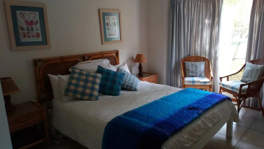 Queen bedroom with cane headboard chairs, blue throw and garden-facing doors
