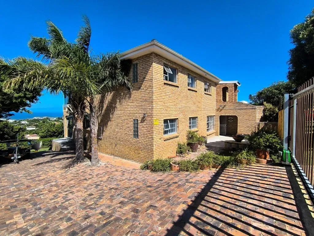 Double-storey brick house with a paved driveway, palm tree and gated parking court, sea visible beyond