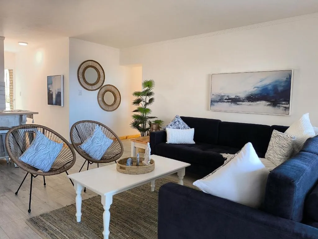 Living room with navy blue sofas, woven papasan chairs, round rattan mirrors and abstract wall art