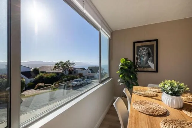 Sunlit breakfast nook beside a floor-to-ceiling window looking over rooftops to the sea and mountains