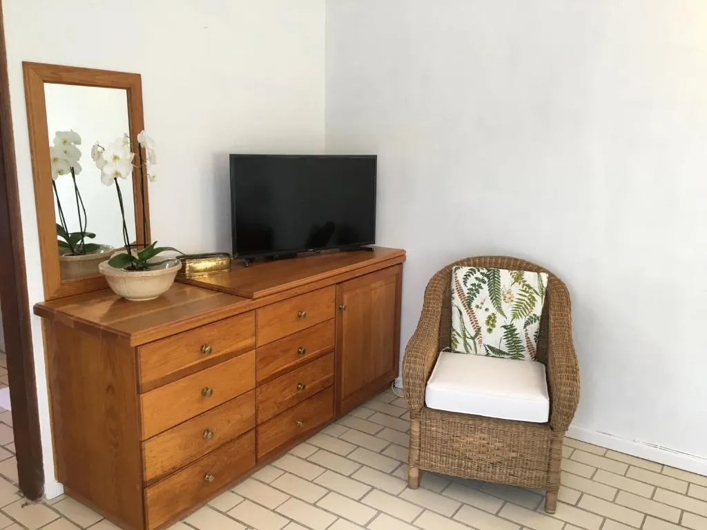 Bedroom with a wooden dresser, mirror and a wicker armchair on tiled flooring