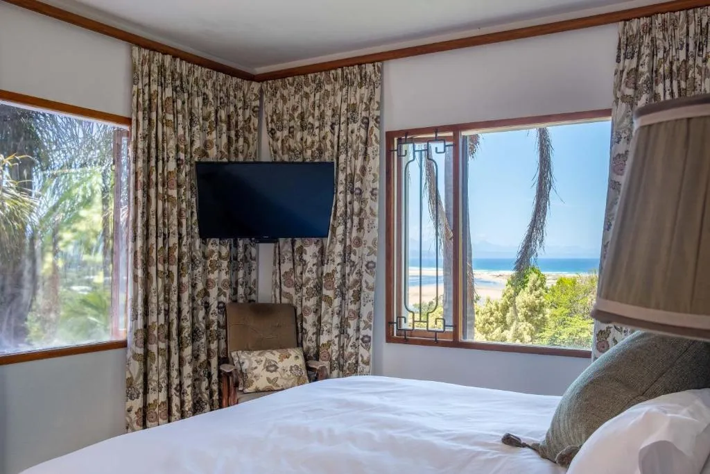 Bedroom with floral curtains and a window framing the Keurbooms lagoon and sea beyond