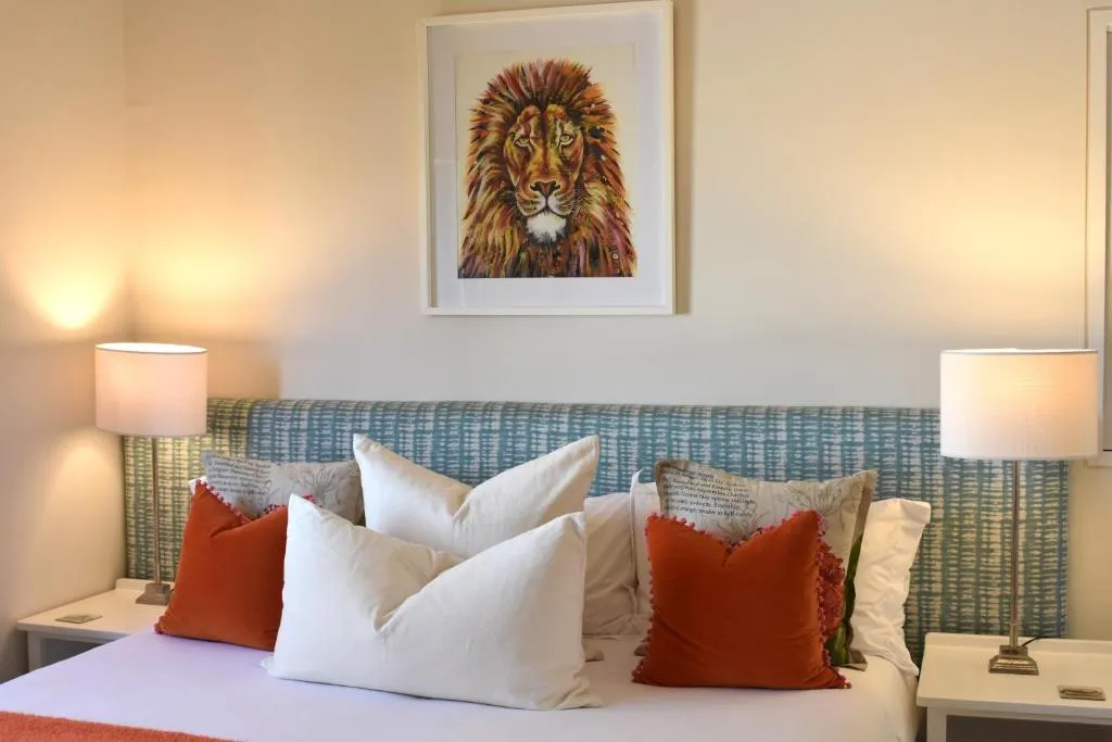 Headboard styled with an ochre lion artwork above rust and cream scatter cushions and bedside lamps