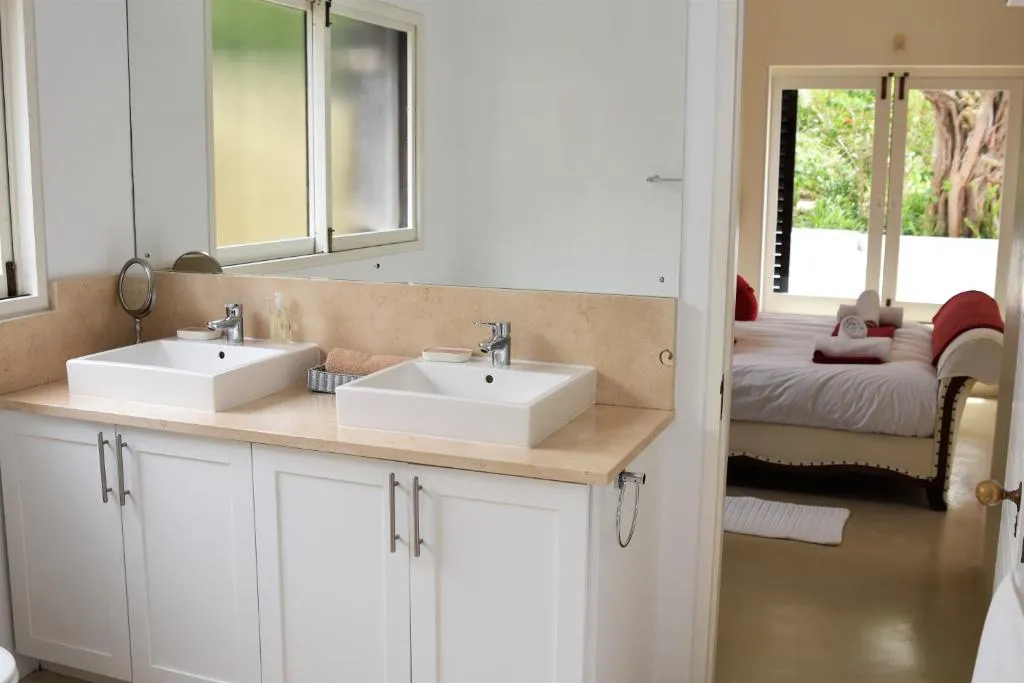 Double-basin en-suite vanity opening directly onto a bedroom with a carved daybed and garden doors