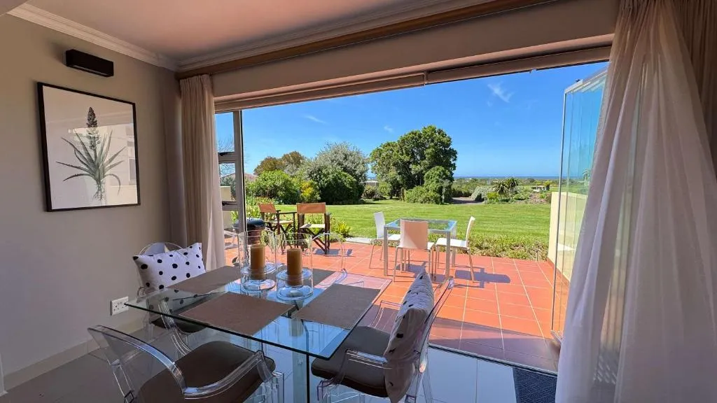 Dining table beside floor-to-ceiling windows framing a distant sea view over the garden