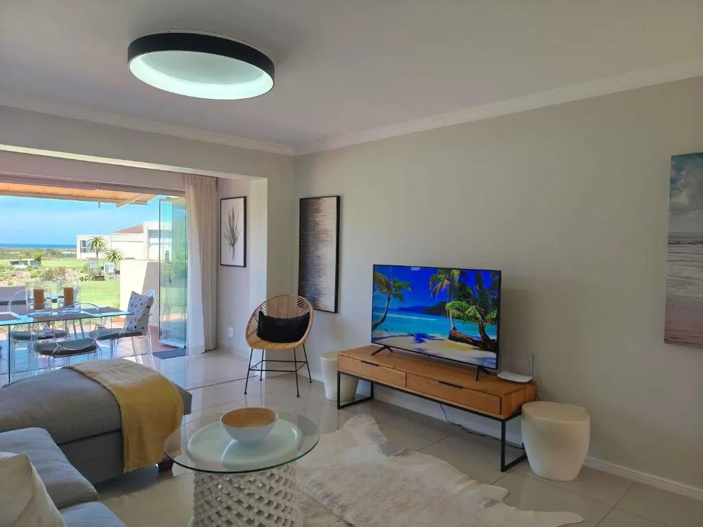 Living room with a wall-mounted TV, rattan chair and glimpses of the sea and palm trees through open doors