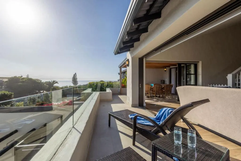 Covered balcony with sun loungers and a glass balustrade overlooking the sea in the distance