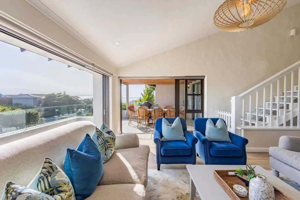 Open-plan living room with blue armchairs opening onto a covered terrace with a distant sea view