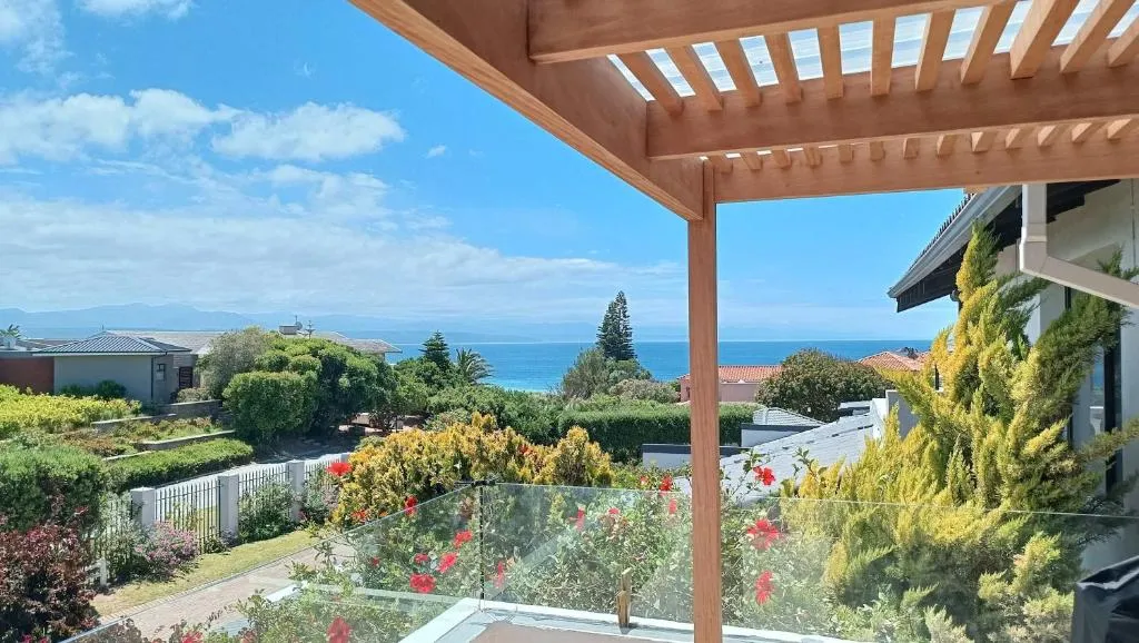 Sea view from a wooden pergola-covered balcony surrounded by flowering shrubs