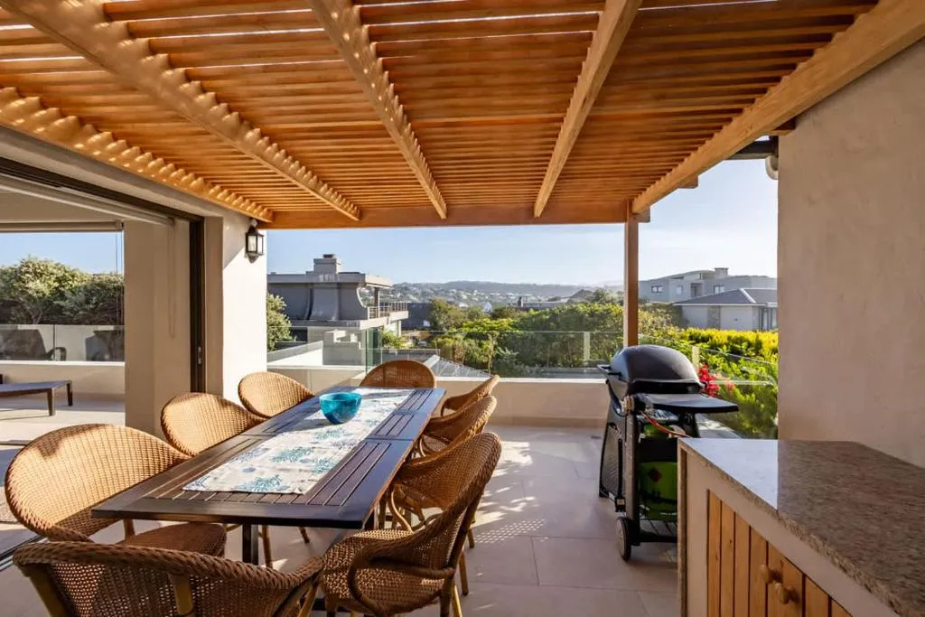 Covered wooden pergola terrace with a dining table and gas braai overlooking the hills
