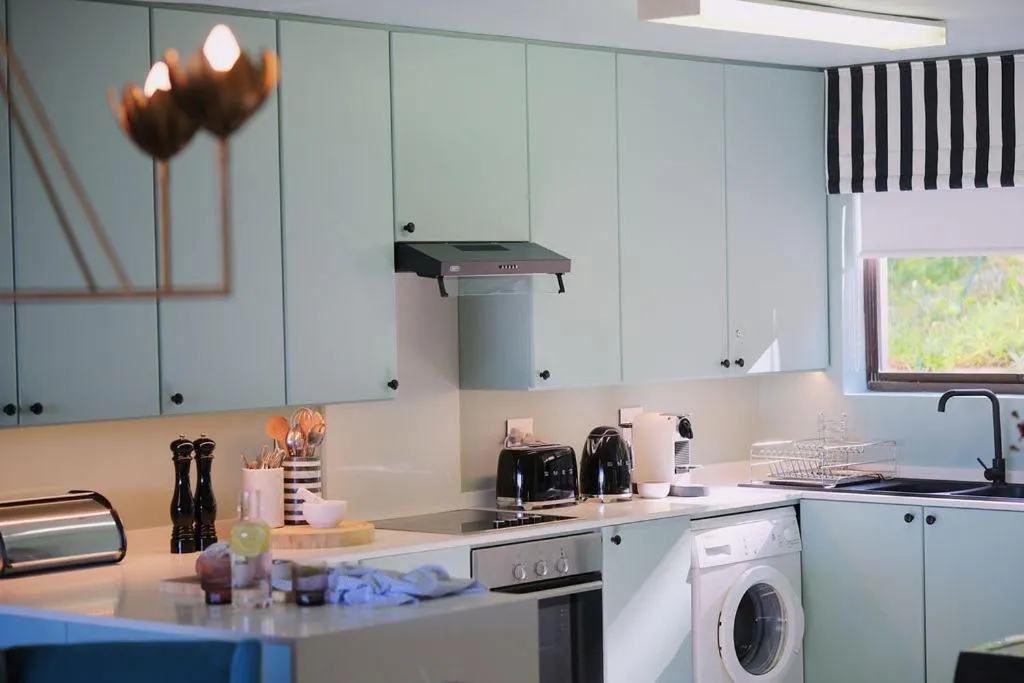 Mint-green kitchen cabinetry with an oven, hob and a front-loading washing machine below the counter