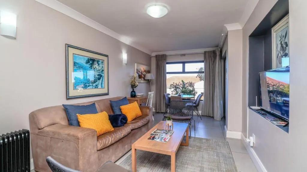 Living room with a tan leather sofa, mustard cushions and a dining nook by the window