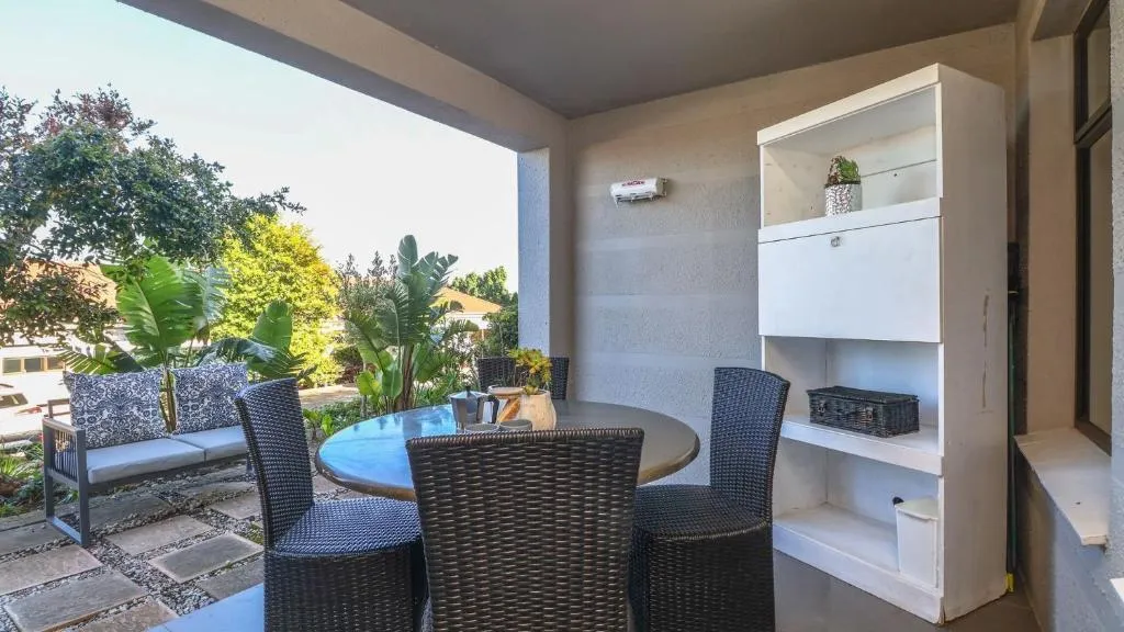 Covered patio with a wicker dining set and lounge seating among potted palms
