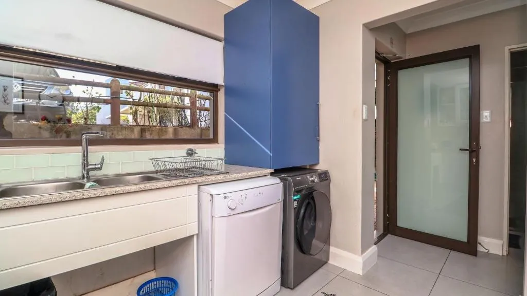 Scullery with a stacked washing machine and dishwasher beside a window over the sink