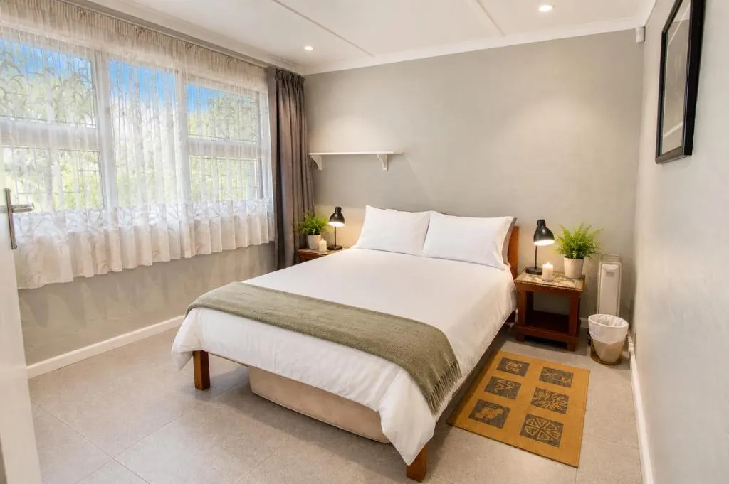 Bedroom with crisp white bedding, sheer curtains, and natural light through a large window