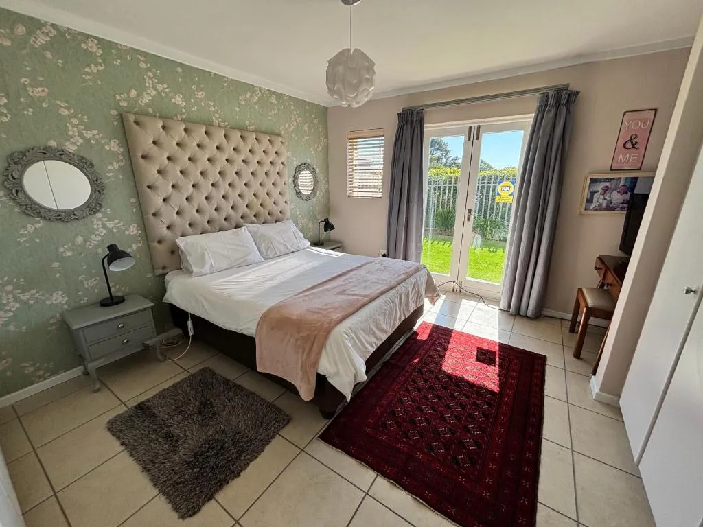 Main bedroom with a tufted grey headboard and glass doors opening onto a small garden