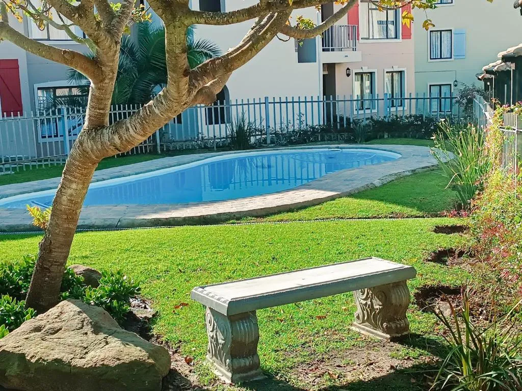 Communal pool and lawned garden shared by the Santini Village estate, seen past a stone bench