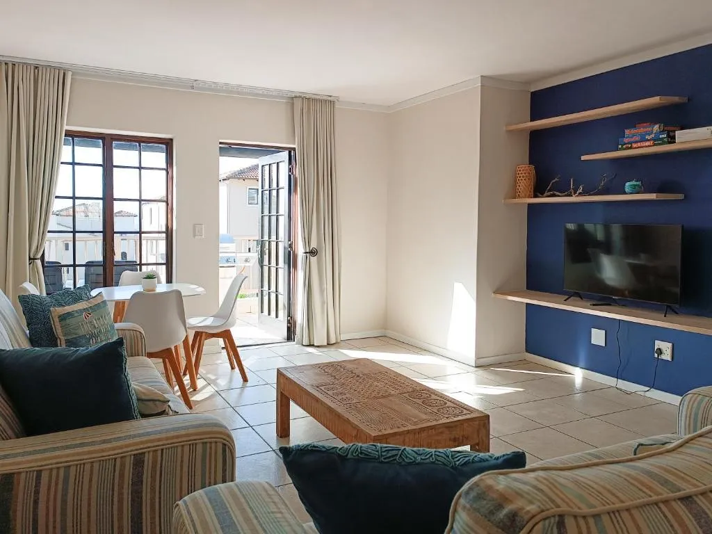 Living room with striped seating, a blue feature wall and doors open to a furnished balcony