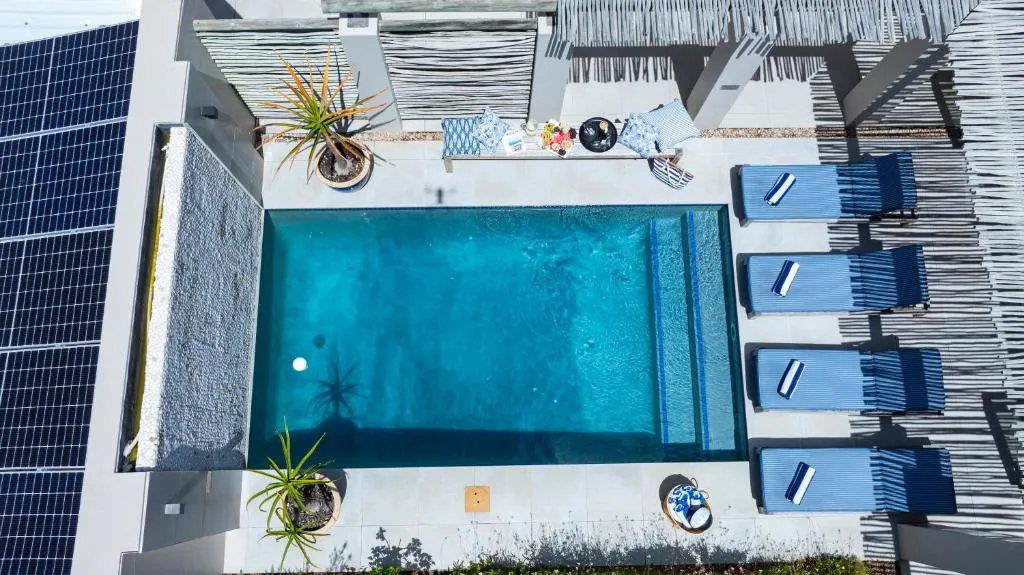 Aerial view of the rectangular pool and sun loungers beside the house's solar panels
