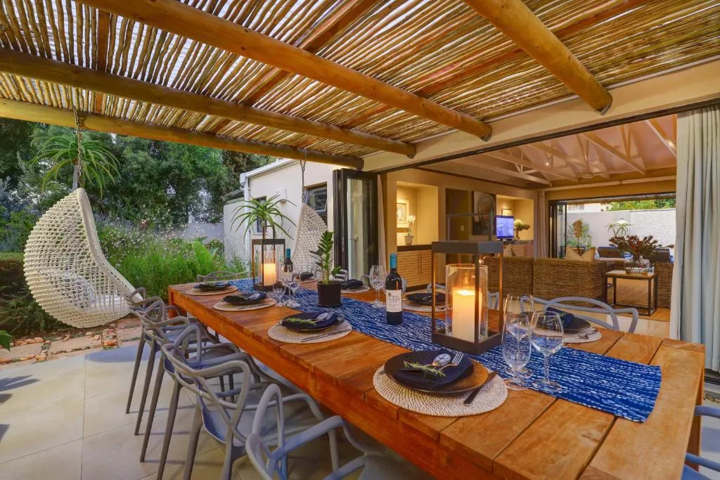 Covered outdoor dining area under a reed pergola, with a long table and a hanging egg chair