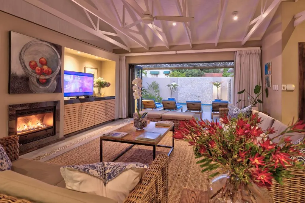 Living room with a lit fireplace and glass doors framing the pool loungers outside
