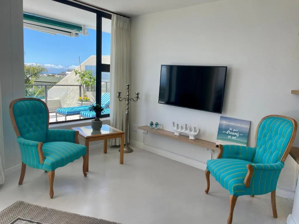 Lounge seating area with teal armchairs, wall-mounted TV and balcony sea view beyond