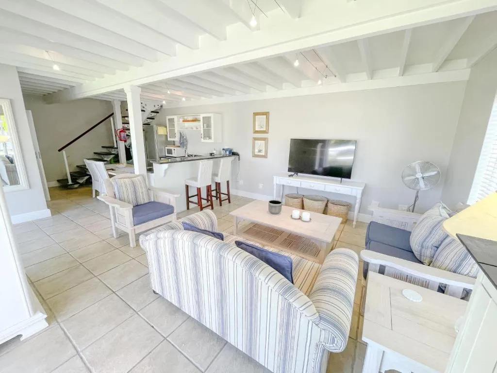 Lounge with striped sofas, TV console and a kitchenette bar beneath an open loft staircase