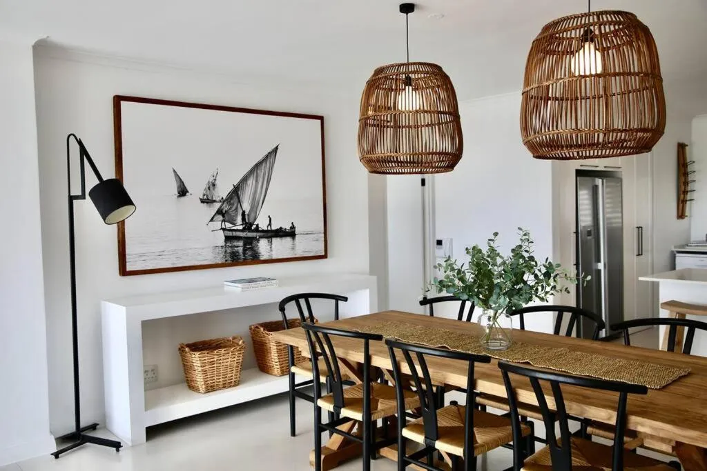 Open-plan dining area with a wooden table, rattan pendant lights and a framed sailing print