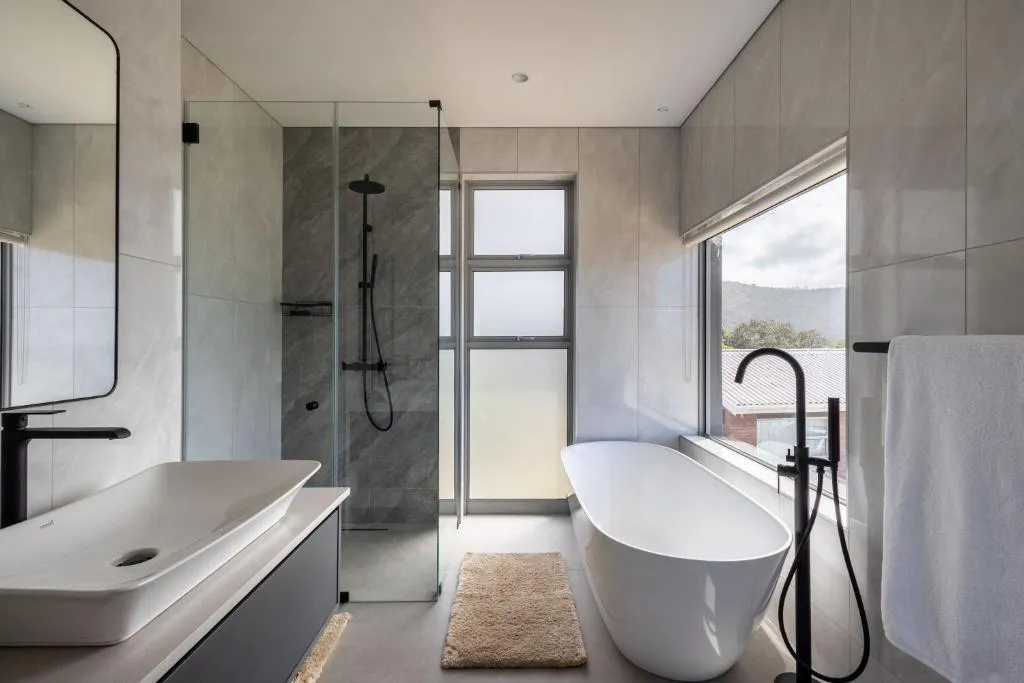 Bathroom with a freestanding tub beneath a hillside-view window and a walk-in glass shower