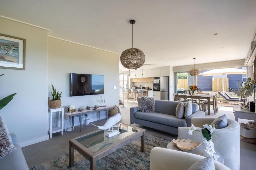 Open-plan lounge and dining area with a wall-mounted TV and glass doors onto the deck