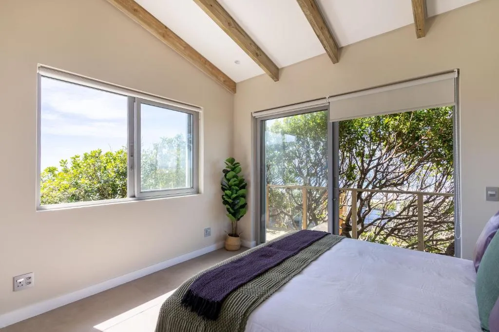 Vaulted-ceiling bedroom with sliding doors opening onto a tree-shaded balcony