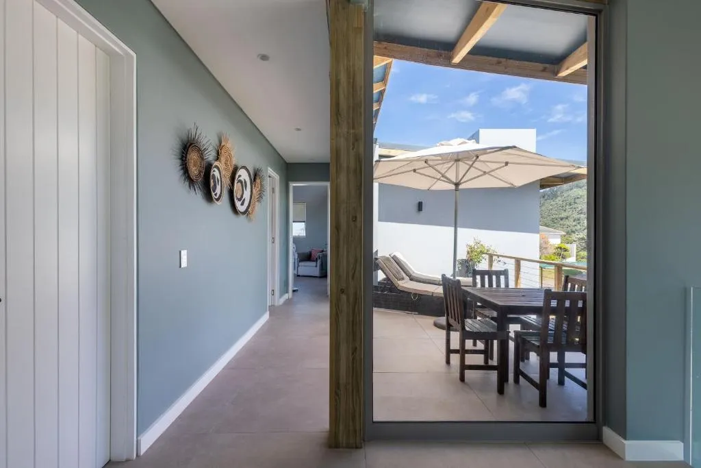 Hallway opening onto a covered terrace with an umbrella-shaded dining table and loungers