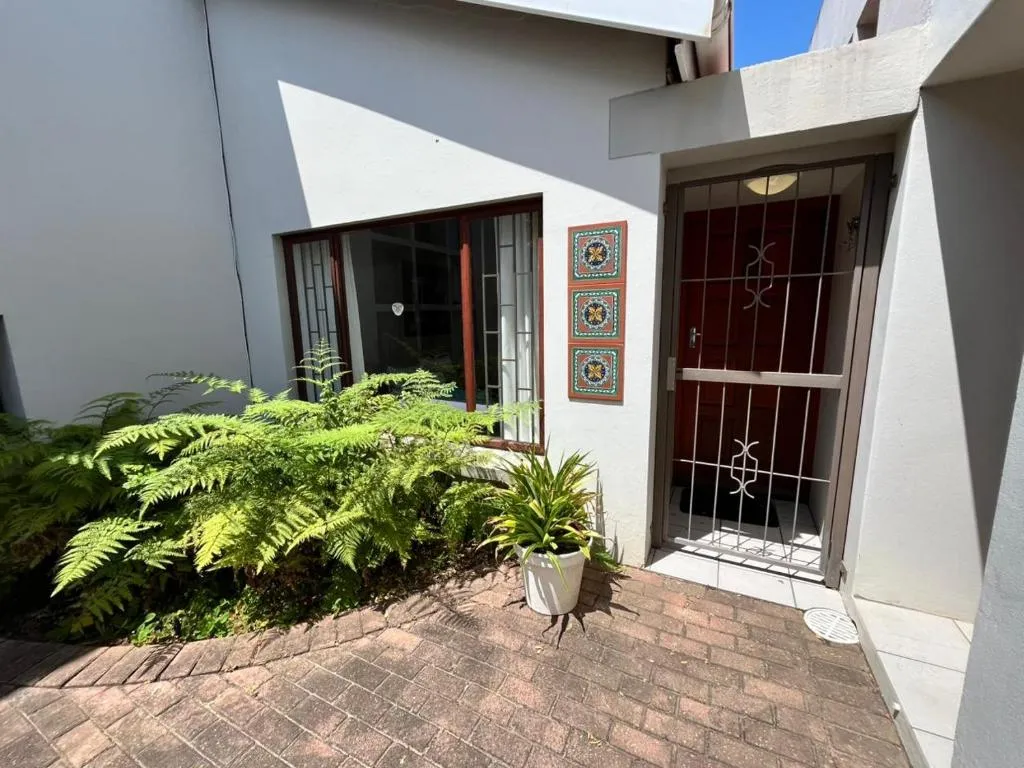 Front entrance with a security gate, dark wood door and ferns in the paved courtyard