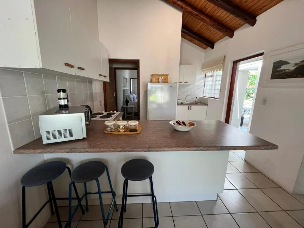 Kitchen with a breakfast bar, three stools and a wood-beam ceiling, opening onto the garden
