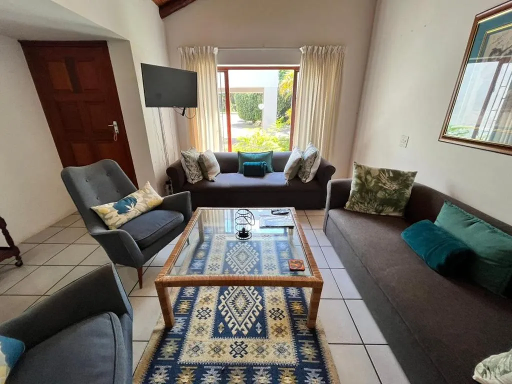 Living room with charcoal sofas and an armchair around a glass coffee table, glass door onto the garden